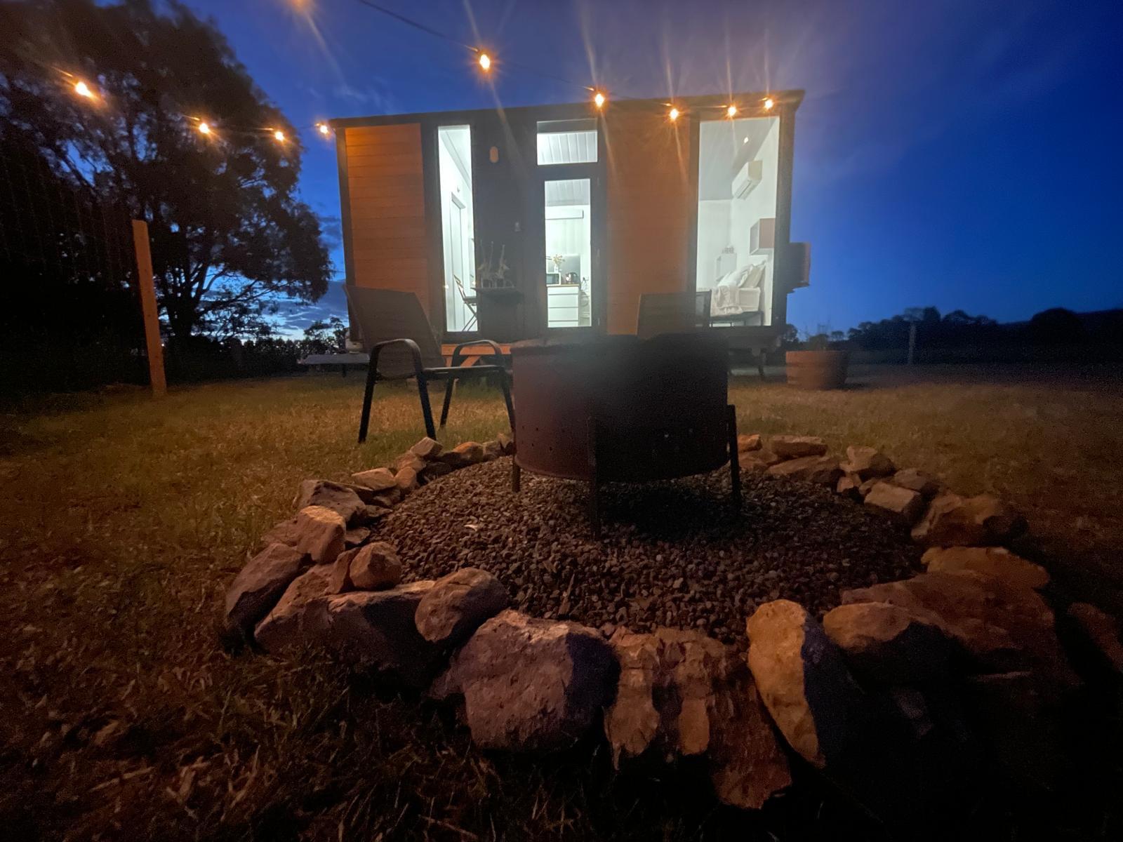 Tiny home lit at night beside a firepit at Midland Meadow.